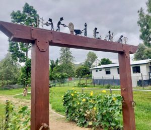 Entrance to the Linville Community Gardens. Wooden square arch way with small metal sculptures on top framing the green garden.