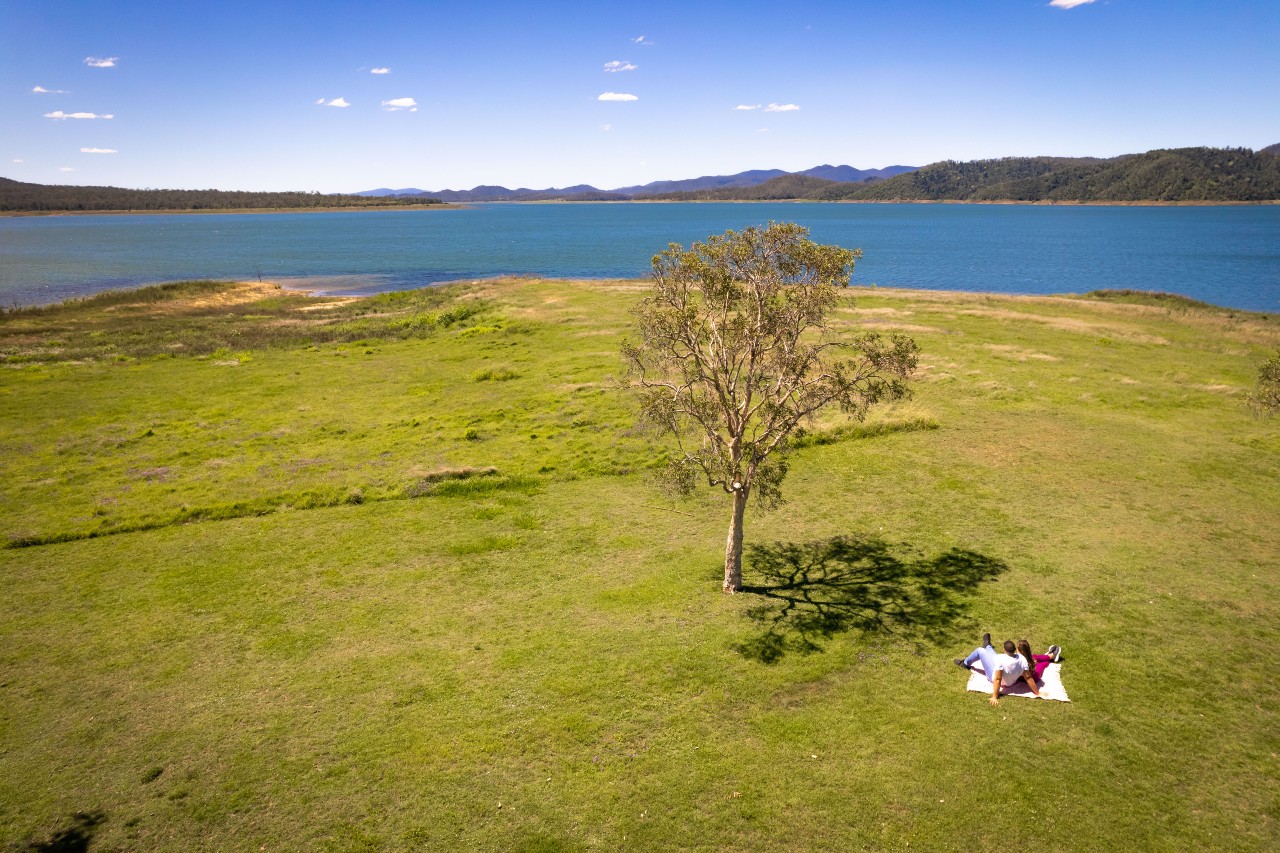 A couple on a picnic blanket sit on the lawn in front of expansive bay