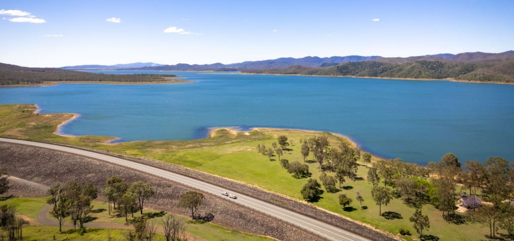 Aerial image featuring long stretch of road beside big blue dam