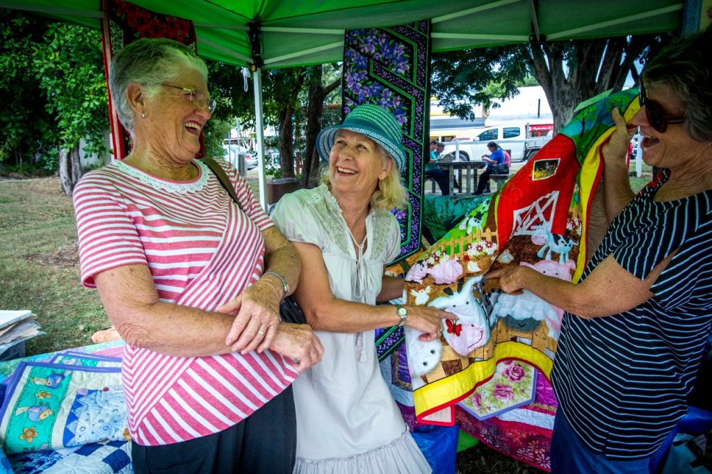 Three women looking at each other smiling and showing goods at the country market