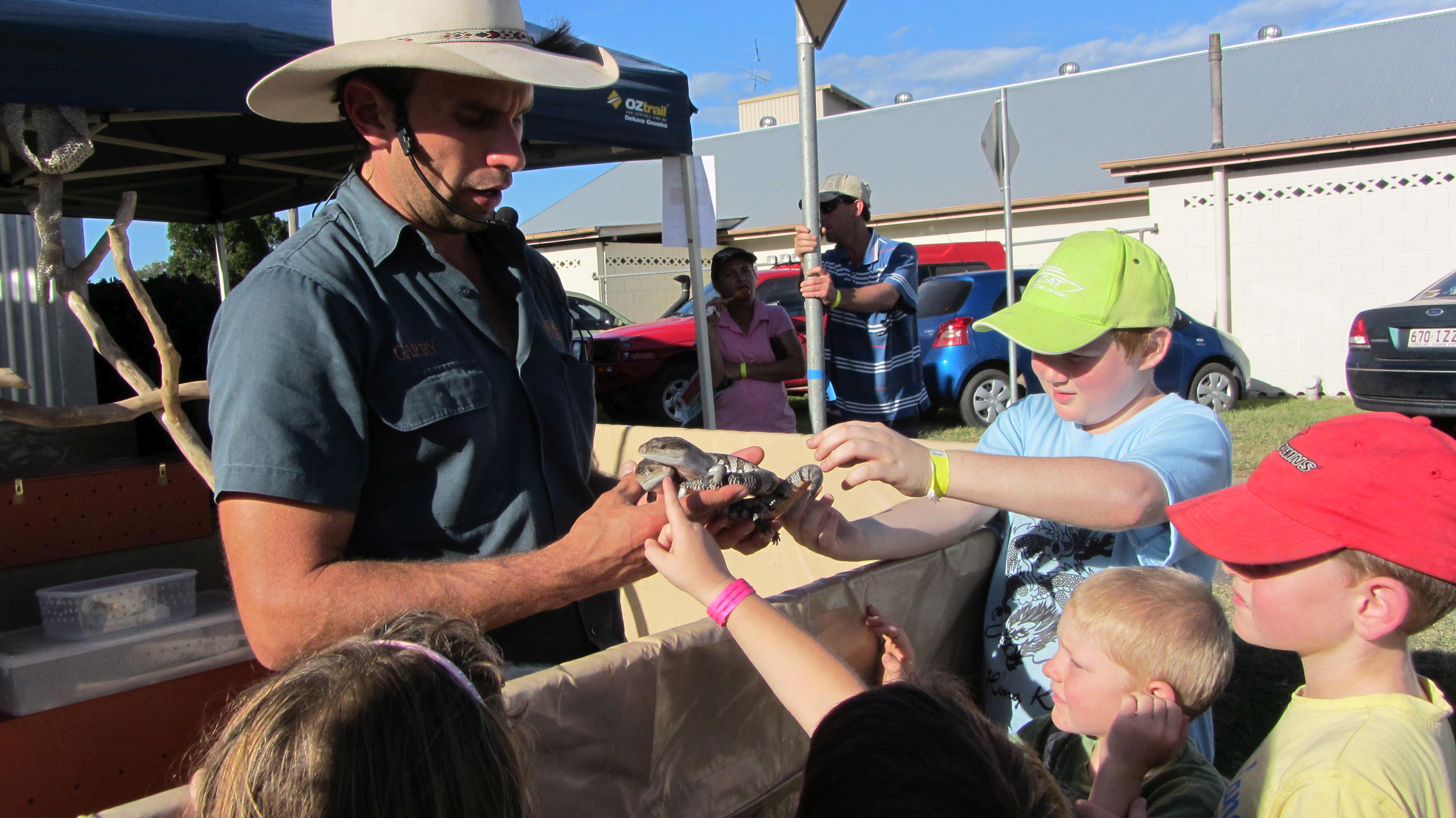 Male presenter holding 2 blue tongue lizards with a group of kids in front patting the lizards and learning about them.