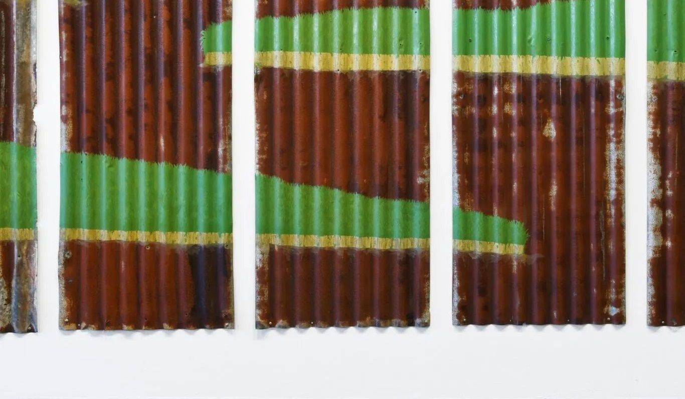 A photograph of Artwork. Pieces of rusted corrugated tin, placed in vertical panels on a white wall. with green painted horizontally on some panels.