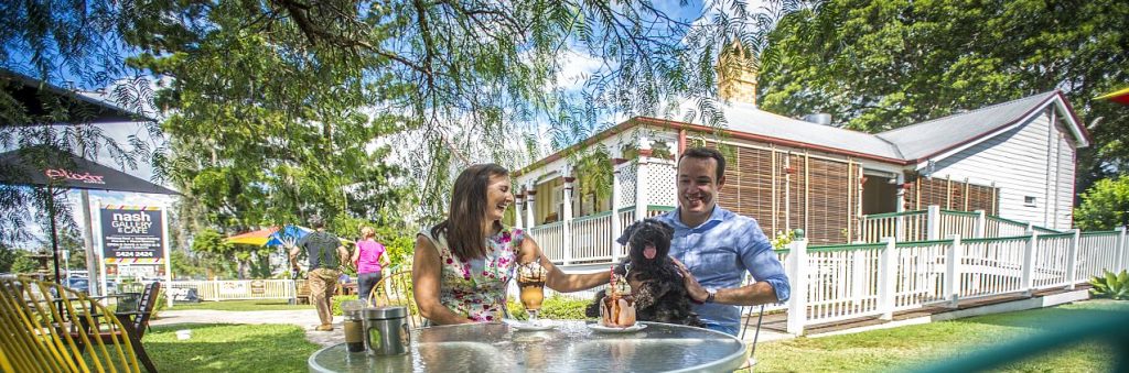 Couple sitting at an outside cafe table with their dog enjoying milkshakes.