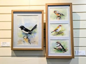 2 rectangular framed pieces of art positioned side by side. The left hand picture is a water colour painting of a black and white will wagtail bird sitting on a branch. The right hand picture is a collection of three water colour finches one above another.