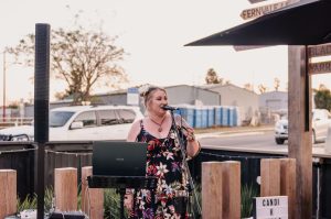 Photo of a singer at a microphone in an outdoor area at a cafe