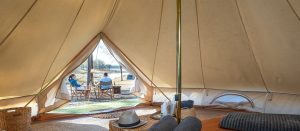 Inside the Glamping tent at Lake Wivenhoe Campgrounds looking out the opening to a couple sitting outside. The bed with towels and centre pole are in view inside.