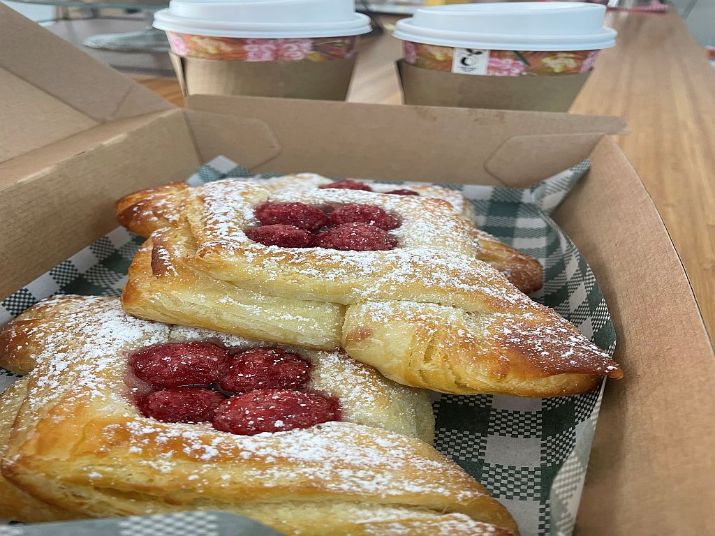 French Pastries (danishes) in a takeaway box, with two takeaway coffee cups in the background.