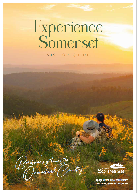 Cover of the Experience Somerset Visitor Guide. A couple watching Golden sunset whilst sitting in the grass over looking the mountains at Jimna.