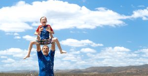 A man holds a child above his head while standing in a lake.