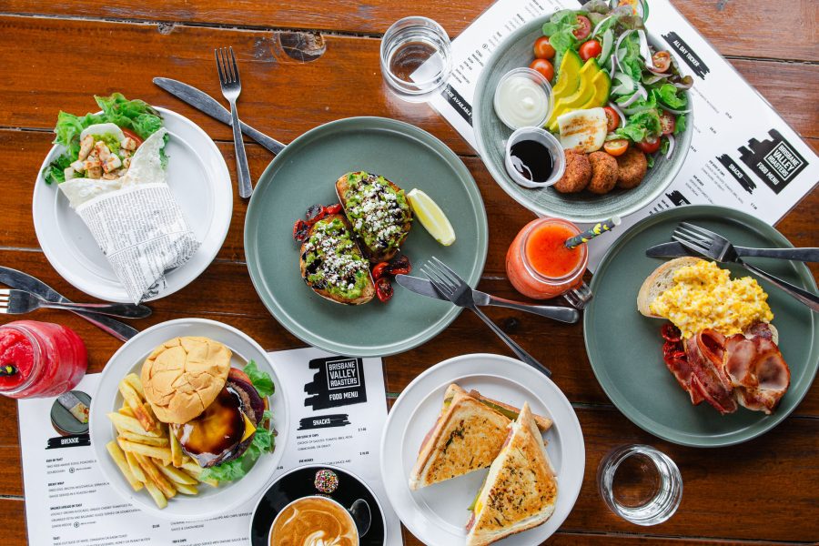 Flat lay photo of the food options at Brisbane Valley Roasters including: Salad wrap, burger and chips, avocado on toast, salad, bacon and eggs and toasted sandwich with coffee