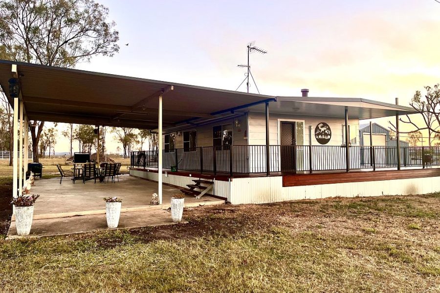 Clarendon Cottage, outside view of the two bedroom cottage. Concrete pathway around the house, with a grassed yard and gum trees in the background.