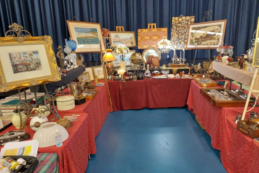 Tables set out in a u- shape covered with a red table cloth with a range of antiques and paintings on display.