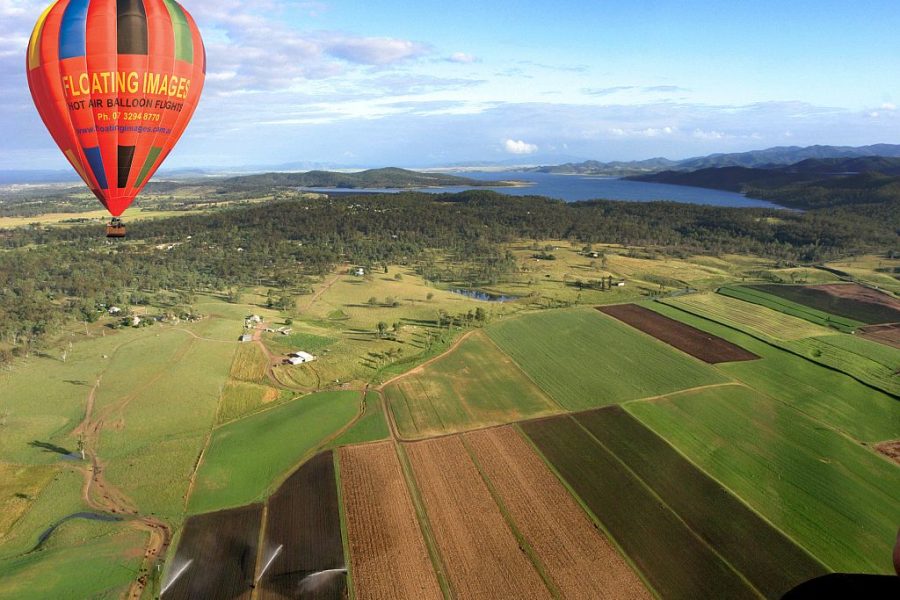 Floating Images Hot Air Balloon Flights - Red hot air balloon with coloured stripes at the top, floating over the green countryside of Somerset with views of Lake Wivenhoe in the distance.