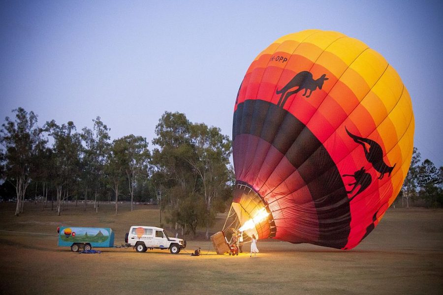 Hot Air Balloon getting getting ready to take off . The red and yellow balloon with kanagroos printed on it, is on its side, filling the balloon with gas from the open flame. A four wheel drive vehicle is parked to the left of the balloon.