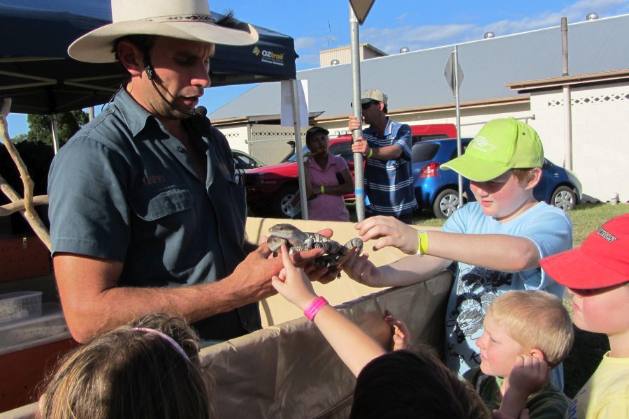 Male presenter holding 2 blue tongue lizards with a group of kids in front patting the lizards and learning about them.