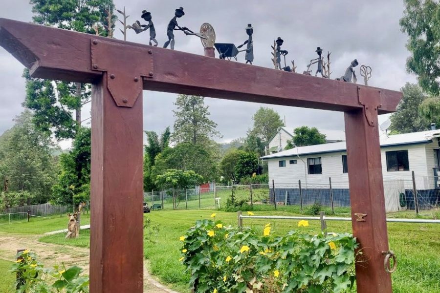 Entrance to the Linville Community Gardens. Wooden square arch way with small metal sculptures on top framing the green garden.