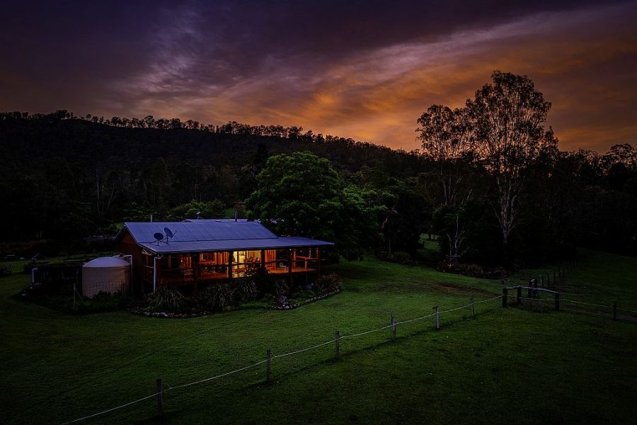 The Log Cabin at Mount Byron Retreat. Photo has been taken in the early evening as its getting dark with lights on. The cabin is surrounded by green grass and trees with a mountain silhouette in the background