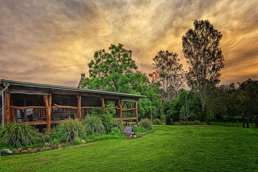 The Log cabin at Mount Byron Retreat, green grass out the front and tall trees in the background. The photo has been taken at sunset with a golden glow in the sky.