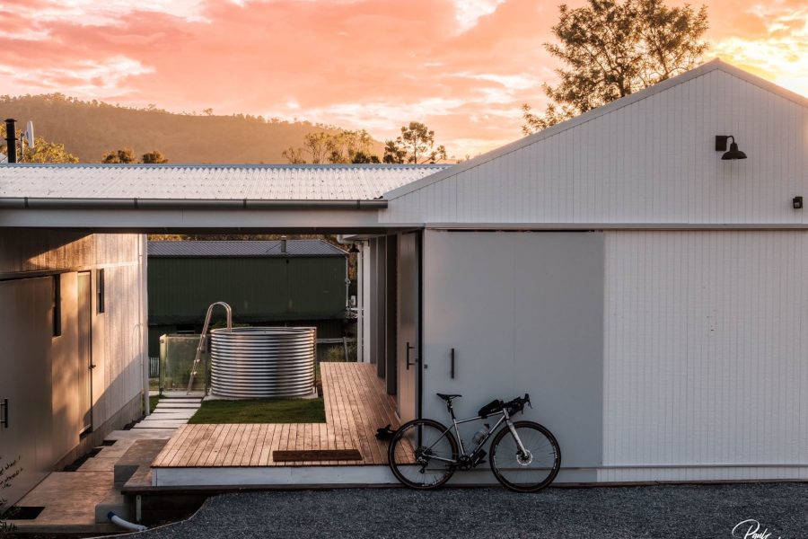 External view of the Rail Trail Refuge at sunrise. A bike leaning on the front white wall. You can see through the covered walkway to the tank plunge pool at the back.