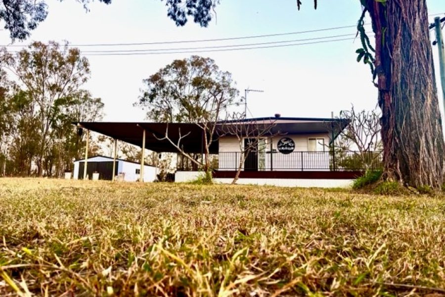 Front view of Clarendon Cottage, with grass in the foreground and trees off to the side and behind the grey cottage.